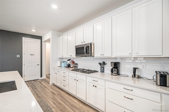 kitchen featuring stainless steel appliances, light stone countertops, light hardwood / wood-style floors, decorative backsplash, and white cabinets