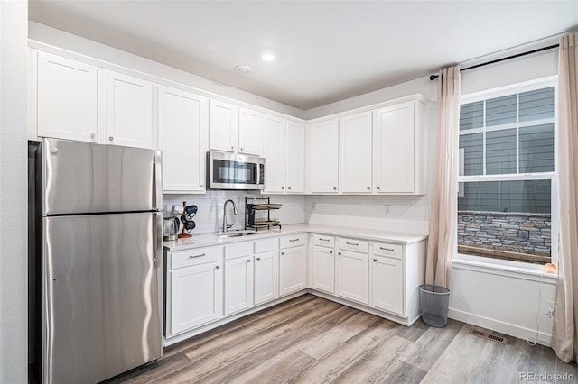 kitchen with sink, white cabinetry, light wood-type flooring, appliances with stainless steel finishes, and backsplash