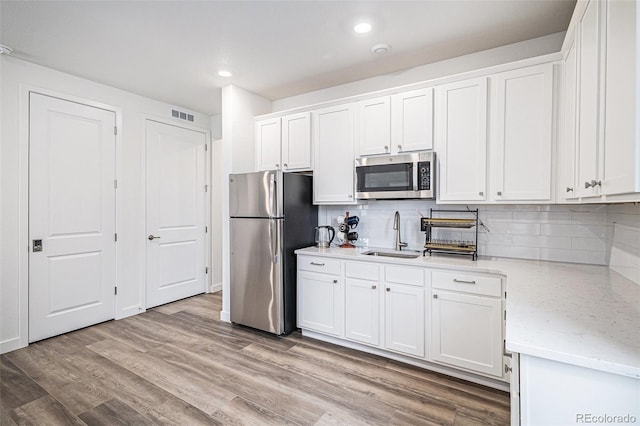 kitchen with sink, tasteful backsplash, appliances with stainless steel finishes, light hardwood / wood-style floors, and white cabinets