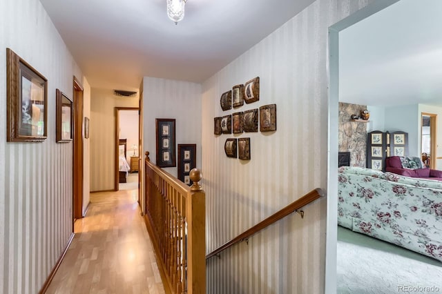hall featuring light wood-style flooring, an upstairs landing, and wallpapered walls