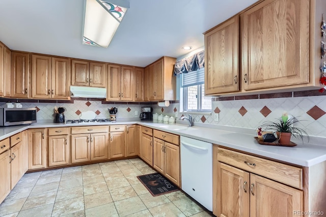 kitchen featuring a sink, tasteful backsplash, under cabinet range hood, and white appliances