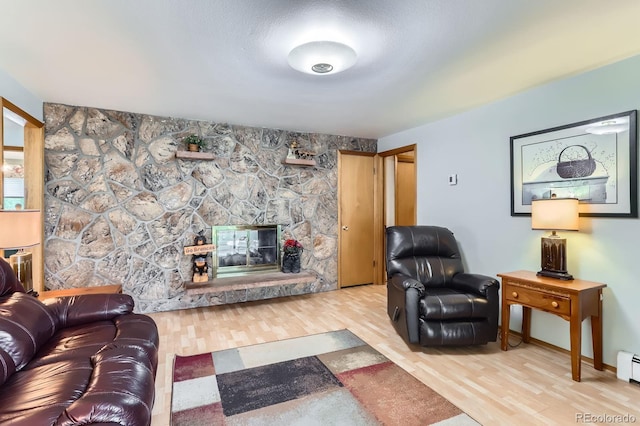 living room with baseboards, baseboard heating, a stone fireplace, and wood finished floors