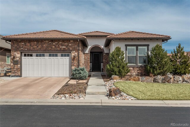 mediterranean / spanish home featuring driveway, a tile roof, stone siding, stucco siding, and an attached garage