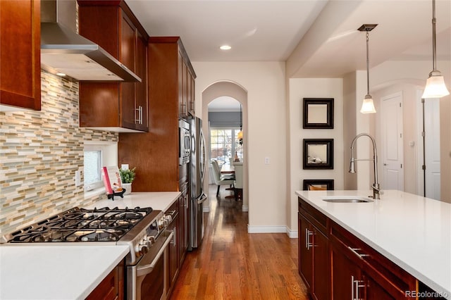 kitchen with decorative backsplash, appliances with stainless steel finishes, wall chimney exhaust hood, sink, and hanging light fixtures