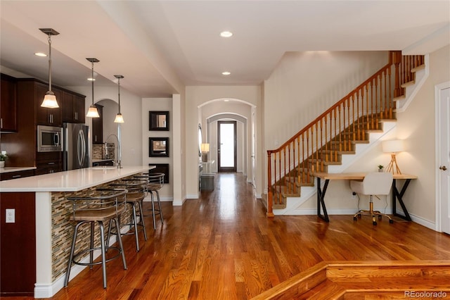 kitchen with appliances with stainless steel finishes, a breakfast bar, dark brown cabinetry, dark hardwood / wood-style floors, and hanging light fixtures