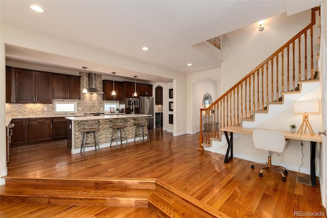 kitchen with dark wood-type flooring, a center island with sink, wall chimney exhaust hood, and a breakfast bar area