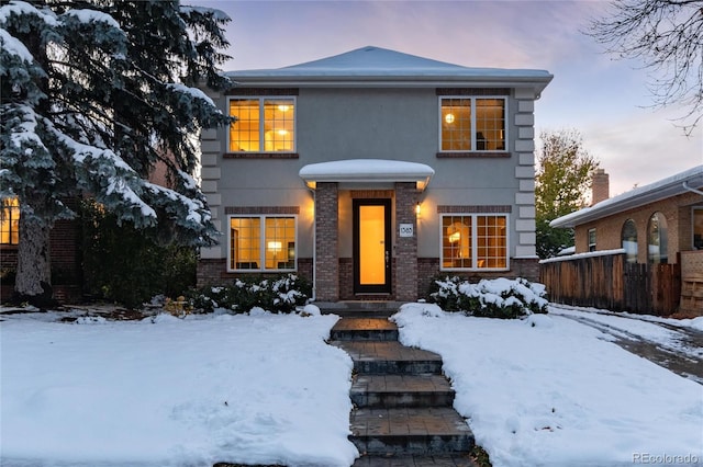 view of front facade featuring stucco siding, brick siding, and fence