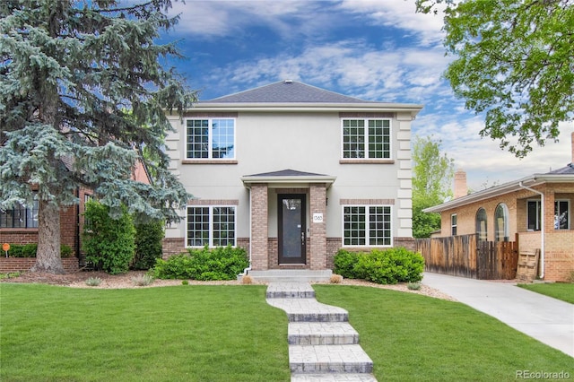 view of front of house with brick siding, stucco siding, a front yard, and fence