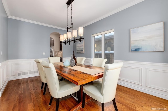 dining room featuring a wainscoted wall, arched walkways, dark wood finished floors, visible vents, and ornamental molding