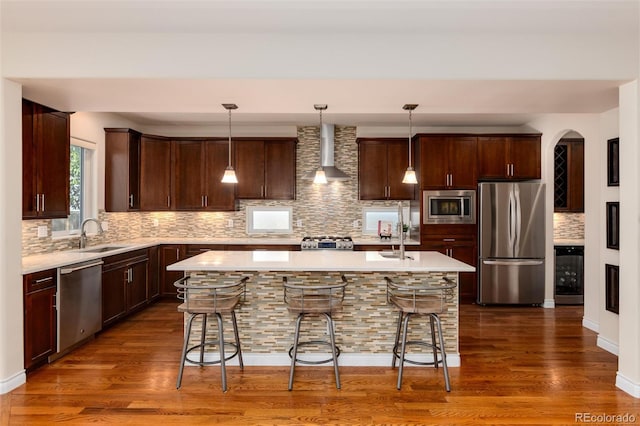 kitchen featuring tasteful backsplash, a breakfast bar area, stainless steel appliances, light countertops, and wall chimney exhaust hood