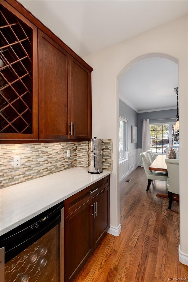 bar featuring tasteful backsplash, wood finished floors, arched walkways, ornamental molding, and wine cooler