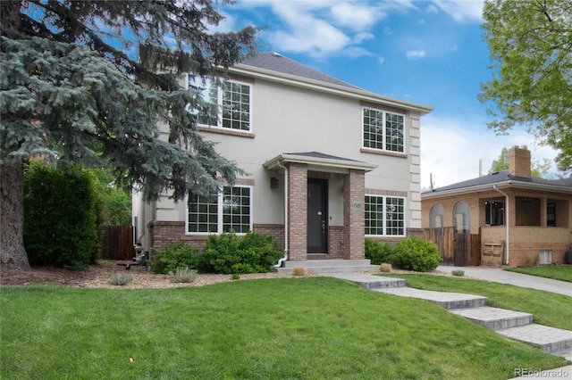 view of front of house featuring brick siding, stucco siding, a front yard, and fence