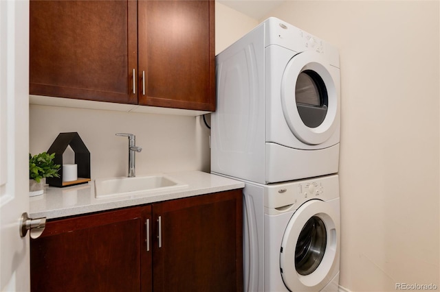 laundry area featuring stacked washer and clothes dryer, a sink, and cabinet space