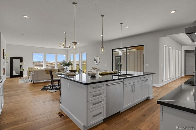 kitchen featuring a kitchen island with sink, sink, stainless steel dishwasher, white cabinets, and light hardwood / wood-style floors