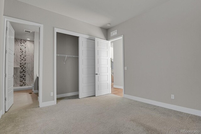 unfurnished bedroom featuring a closet, light colored carpet, and ensuite bath