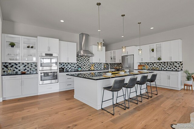 kitchen with white cabinetry, tasteful backsplash, stainless steel appliances, wall chimney exhaust hood, and light hardwood / wood-style floors