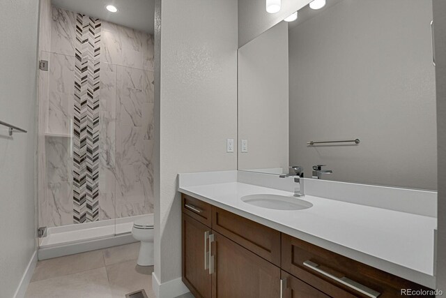 bathroom featuring tile patterned flooring, toilet, a tile shower, and vanity