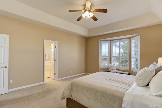 bedroom featuring light colored carpet, a raised ceiling, ceiling fan, and ensuite bathroom