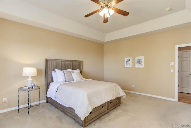 bedroom featuring a raised ceiling, light carpet, and ceiling fan