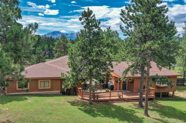 rear view of property with a deck with mountain view and a yard