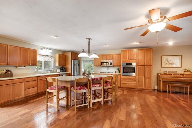 kitchen featuring hanging light fixtures, a kitchen island, stainless steel appliances, ceiling fan, and light hardwood / wood-style flooring