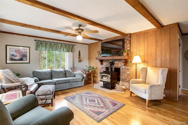 living room with wood walls, beamed ceiling, a wood stove, ceiling fan, and hardwood / wood-style floors