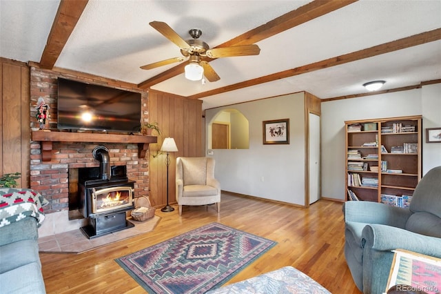 living room with light hardwood / wood-style floors, beamed ceiling, a wood stove, a textured ceiling, and ceiling fan