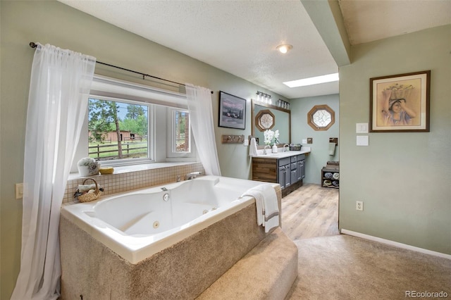 bathroom featuring a textured ceiling, hardwood / wood-style flooring, a bathtub, a skylight, and vanity