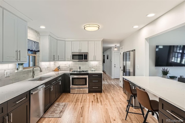 kitchen featuring white cabinets, stainless steel appliances, sink, backsplash, and light hardwood / wood-style flooring