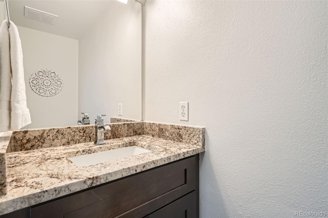 bathroom with a textured wall, visible vents, and vanity