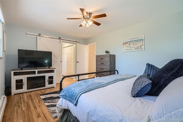 bedroom with light wood finished floors, a closet, baseboard heating, a barn door, and ceiling fan