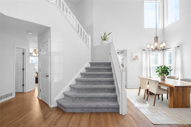 stairs with wood finished floors, a notable chandelier, visible vents, and a towering ceiling