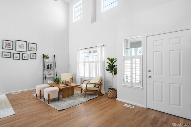 foyer entrance featuring wood finished floors, baseboards, visible vents, and a towering ceiling