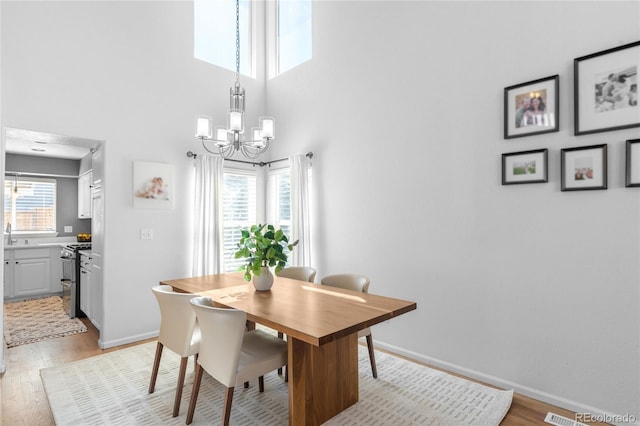 dining area featuring a chandelier, light wood-style floors, baseboards, and a towering ceiling