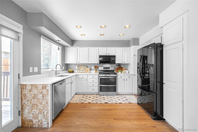kitchen with a sink, light wood-type flooring, black appliances, and white cabinets