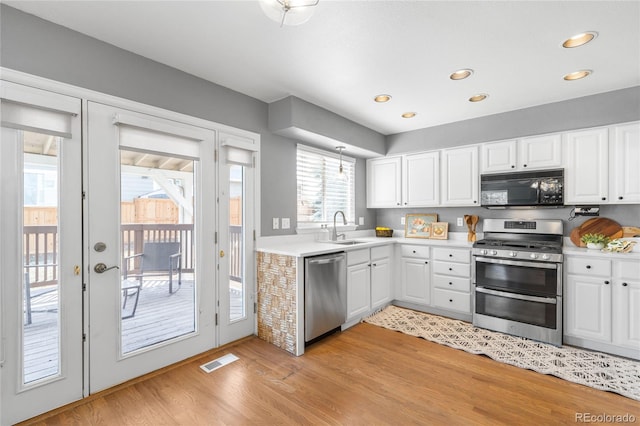 kitchen featuring light wood-type flooring, light countertops, white cabinets, stainless steel appliances, and a sink