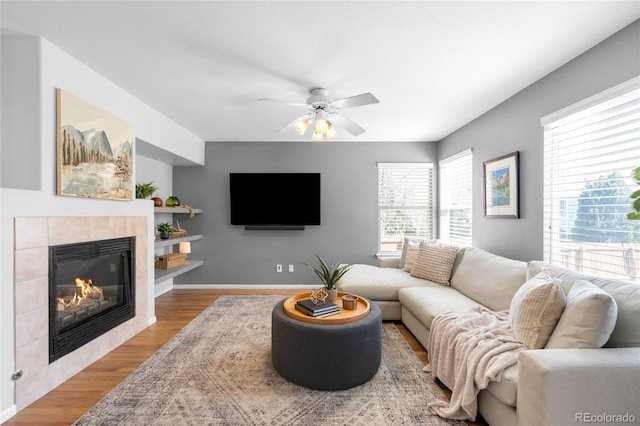 living area with a fireplace, baseboards, a ceiling fan, and wood finished floors