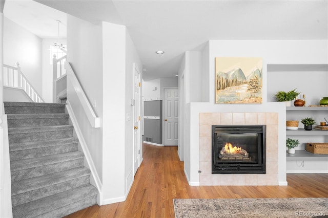 unfurnished living room with a tiled fireplace, baseboards, stairway, and wood finished floors