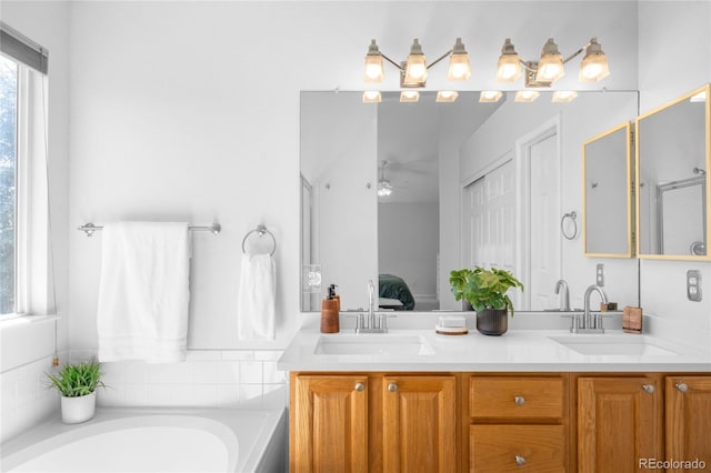 ensuite bathroom featuring a bath, double vanity, a sink, and a ceiling fan