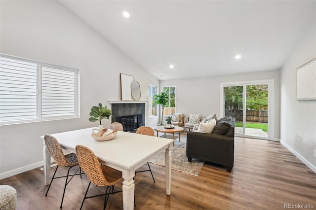 dining area with high vaulted ceiling, dark hardwood / wood-style flooring, and a tile fireplace