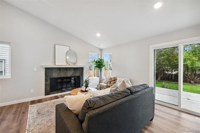 living room featuring lofted ceiling, plenty of natural light, light hardwood / wood-style floors, and a tiled fireplace