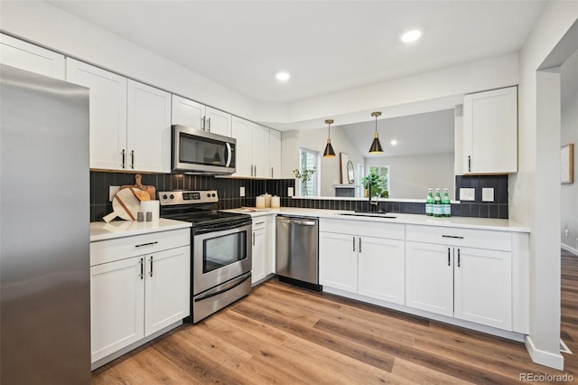 kitchen featuring light wood-type flooring, pendant lighting, white cabinetry, appliances with stainless steel finishes, and backsplash