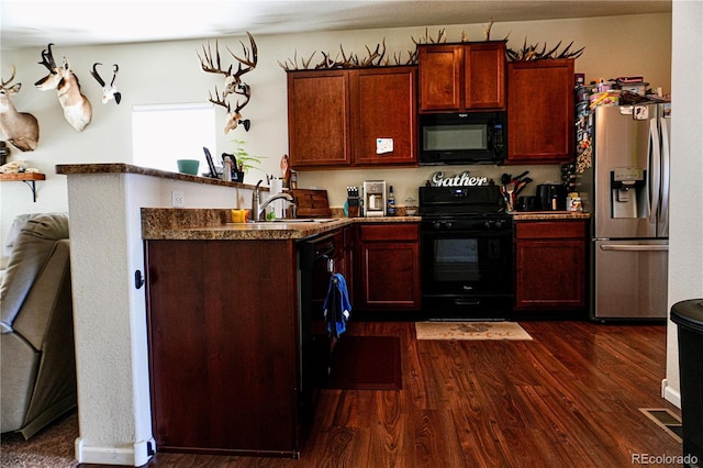 kitchen featuring a peninsula, a sink, dark countertops, dark wood-type flooring, and black appliances