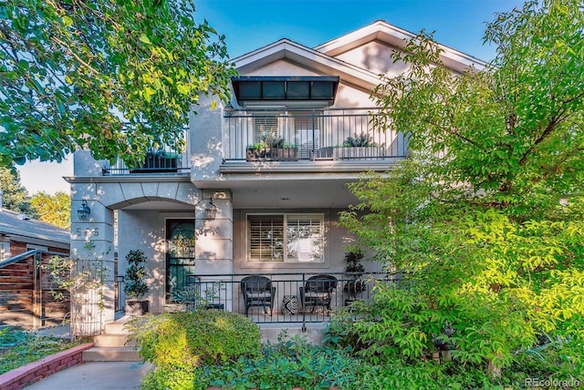 back of property with covered porch, a balcony, and stucco siding