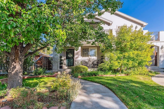 view of property hidden behind natural elements featuring a porch, a front lawn, and stucco siding