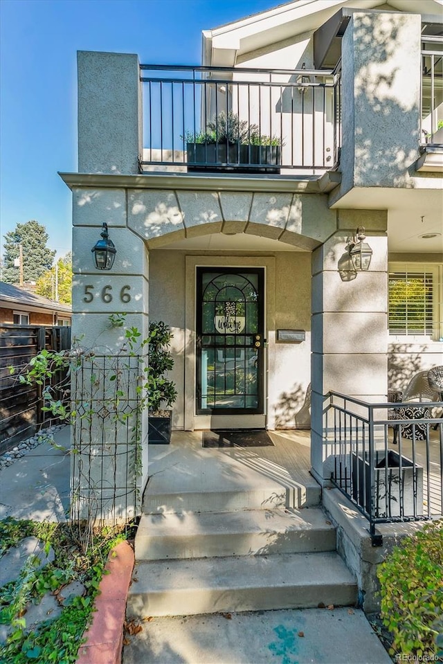 view of exterior entry with a balcony and stucco siding