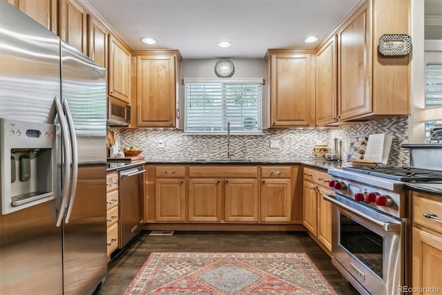 kitchen with decorative backsplash, dark wood-style floors, dark stone countertops, stainless steel appliances, and a sink