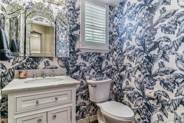 bathroom with toilet, wallpapered walls, and vanity