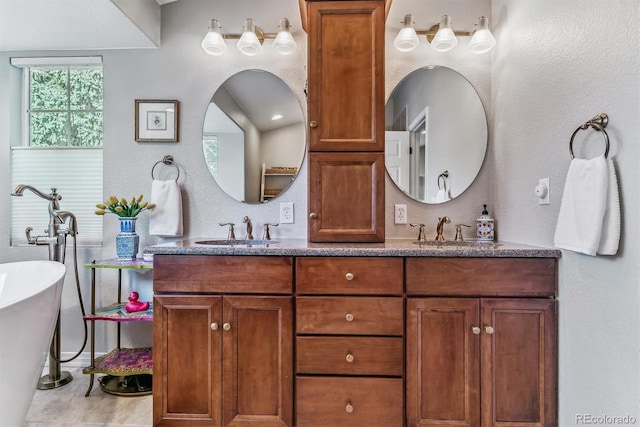 bathroom with a textured wall, a freestanding tub, a sink, and double vanity