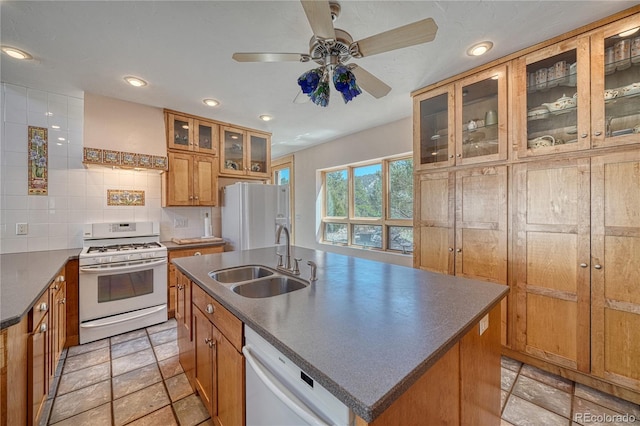 kitchen with a ceiling fan, dark countertops, a sink, brown cabinetry, and white appliances